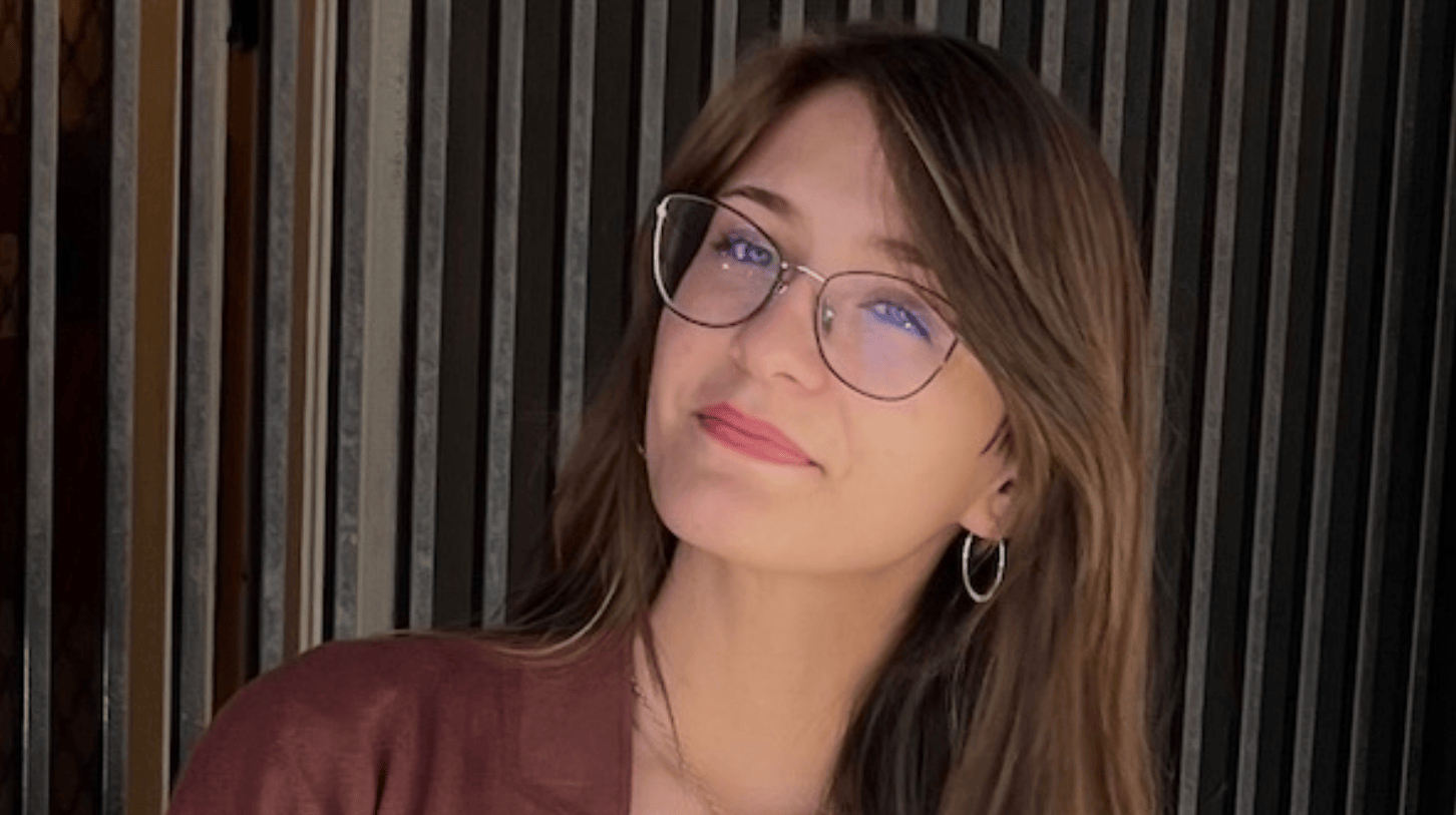 Portrait of a woman with glasses and long hair against a dark textured background